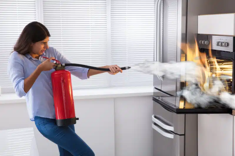 Vrouw blust een brand in haar oven met een brandblusser.
